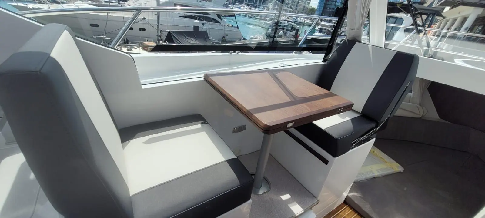 Modern boat interior featuring two stylish seats and a wooden table with a view of yachts at a marina.